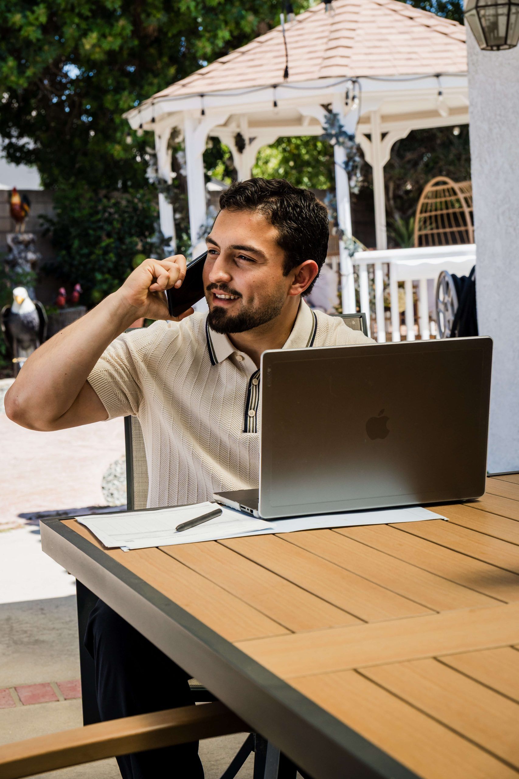 Roberto Valadez smiling on a call at a table under the gazebo